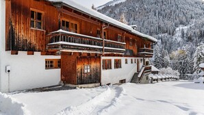 Un chalet de madera con balcón, rodeado de árboles nevados y una montaña al fondo.