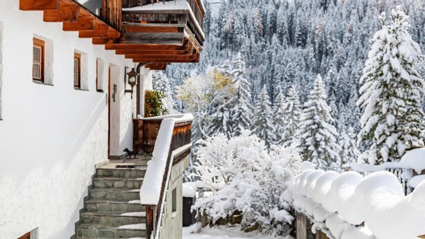 Una escalera de madera que lleva a un balcón con una montaña nevada al fondo.