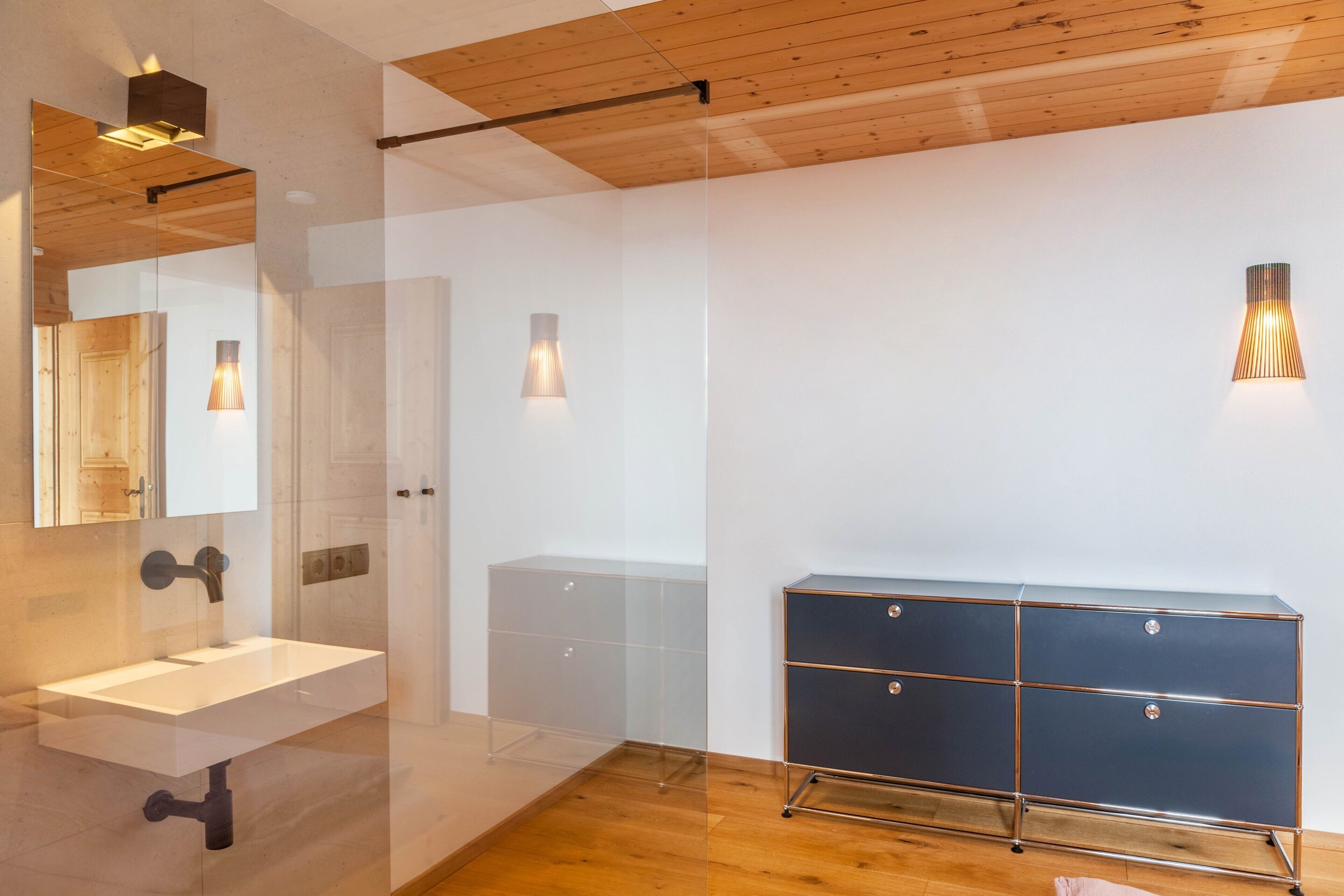 Een moderne badkamer met een glazen douchecabine, een witte wastafel en een donkere houten opbergkast.