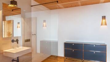 Een moderne badkamer met een glazen douchecabine, een witte wastafel en een donkere houten opbergkast.
