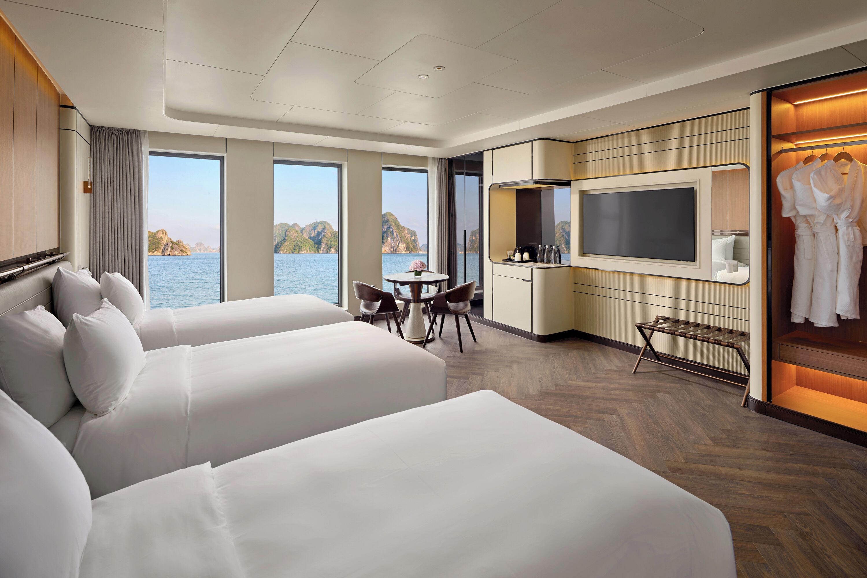 A hotel room with two beds, a dining area, a TV, and a view of the sea.