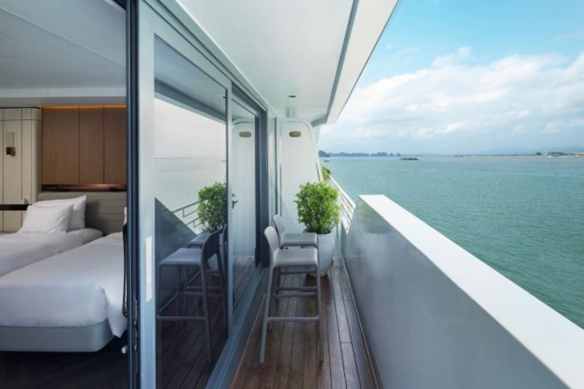 A balcony with a view of the sea, a bed, and a small seating area with a plant.