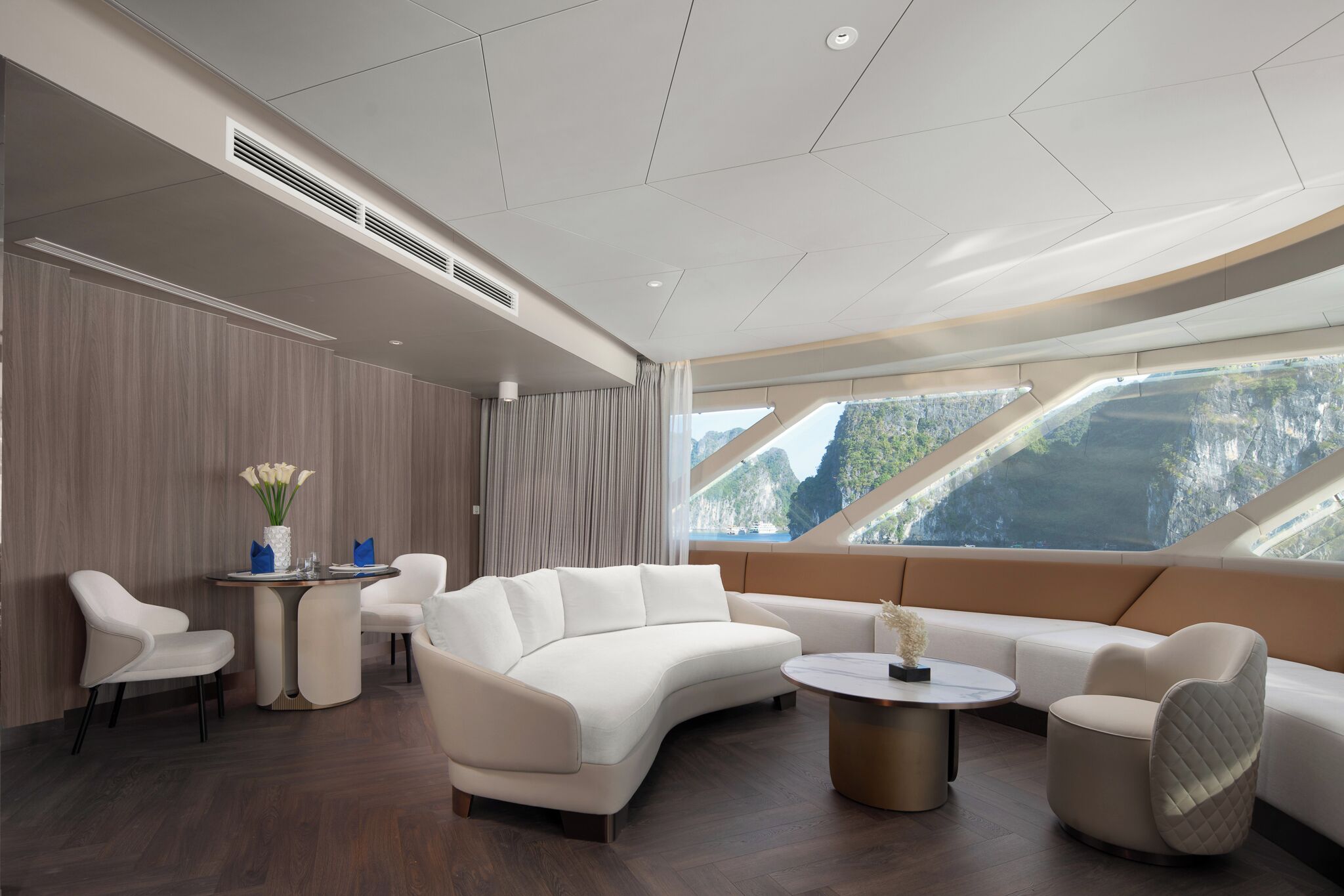 A modern interior with a curved white sofa, a round coffee table, and a view of a mountainous landscape through large windows.