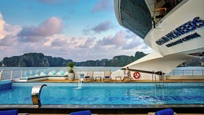 Cubierta de crucero con piscina, sillas de descanso y vista al mar.