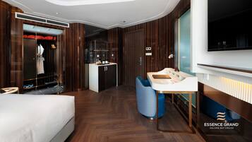 A modern hotel room with a bed, a vanity with a mirror, a seating area, and a wardrobe with a built-in closet.