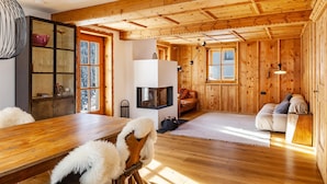 Interior de una cabaña de madera con mesa de comedor, sofá y chimenea.