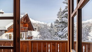 Un balcón de madera con vista a montañas nevadas y un edificio con techo inclinado.