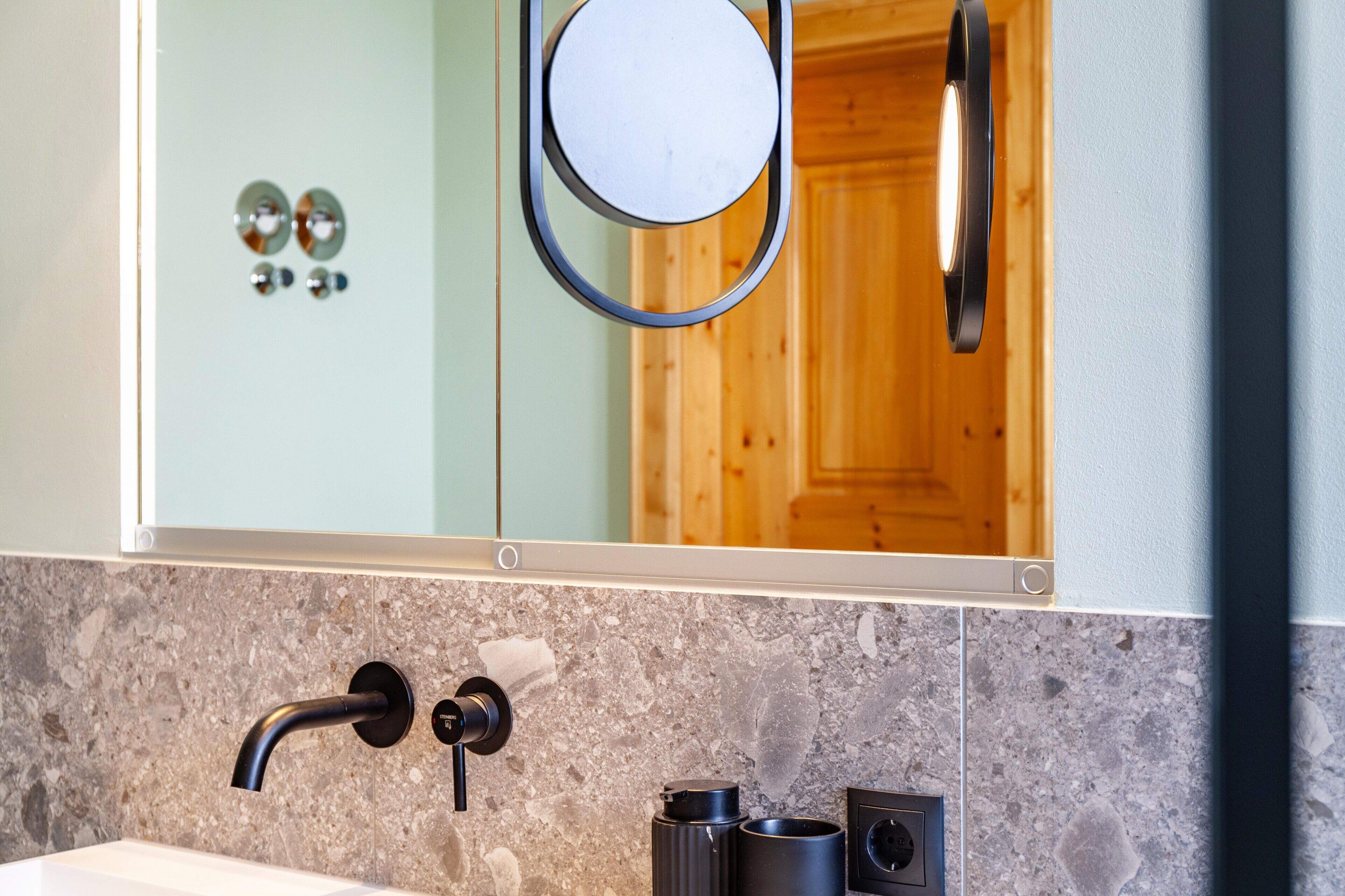 A bathroom with a granite countertop, a black faucet, a mirror, and a wooden door in the background.