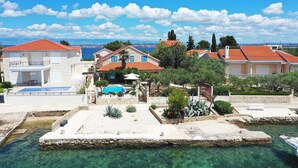 Un quartier résidentiel en bord de mer, avec des maisons, une eau d’un bleu limpide et une piscine.
