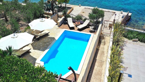 Une piscine avec vue sur la mer, entourée de chaises longues et de parasols.