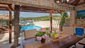 Un espace aménagé au bord de la piscine, avec une table en bois, des chaises et une vue sur la piscine et les montagnes.