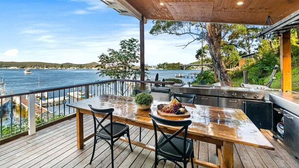 Une terrasse extérieure avec une table et des chaises en bois, un barbecue et une vue sur la mer.