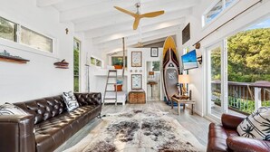 Une pièce spacieuse avec un plafond haut, un canapé en cuir marron, un tapis en peau de vache, une échelle en bois et une planche de surf.