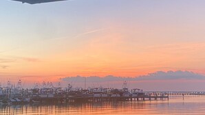 Un port de plaisance où les bateaux sont amarrés aux quais, une eau calme reflétant le coucher de soleil et, au loin, une chaîne de montagnes.