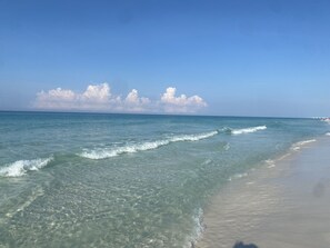 A beach with clear water, gentle waves, and a sandy shore.
