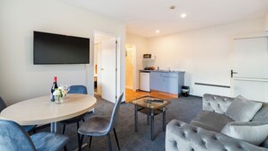 A modern living room with a round table, grey sofa, and a flat-screen TV mounted on the wall. - Daffodil Motel (Christchurch)