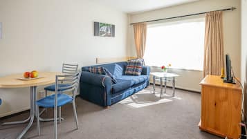 Una habitación con un sofá azul, una mesa redonda con fruta, una mesita redonda con flores y un aparador de madera.
