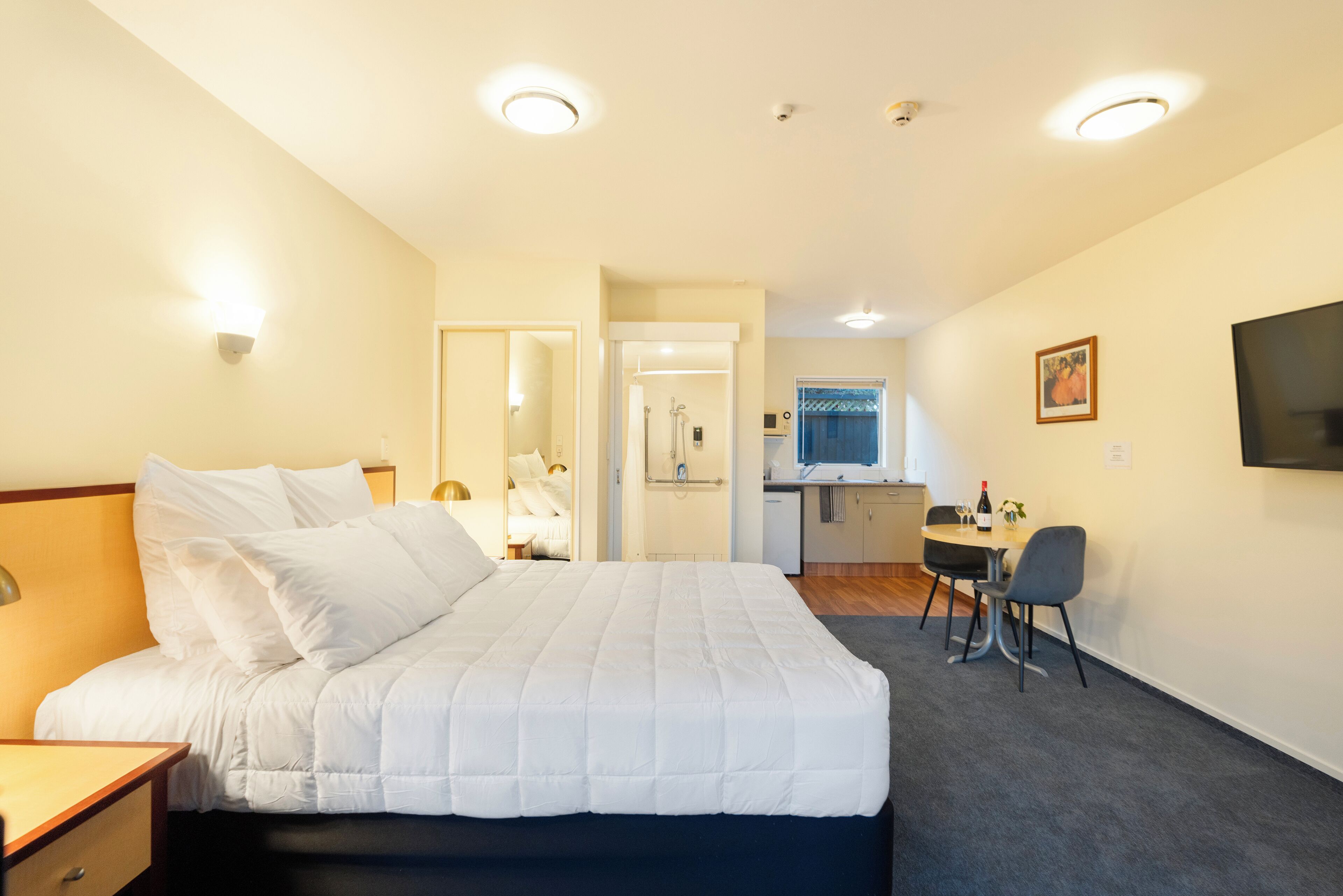 A hotel room with a bed, a desk, and a kitchenette.