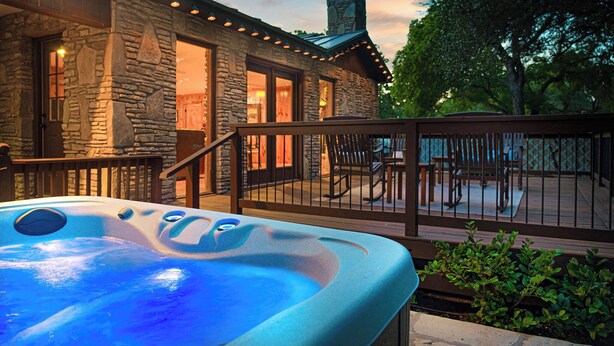 Ein Steinhaus mit Whirlpool auf einer Terrasse, umgeben von Bäumen und einem Holzzaun.