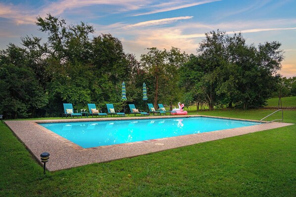 Une piscine rectangulaire bordée de galets, entourée d’une pelouse.