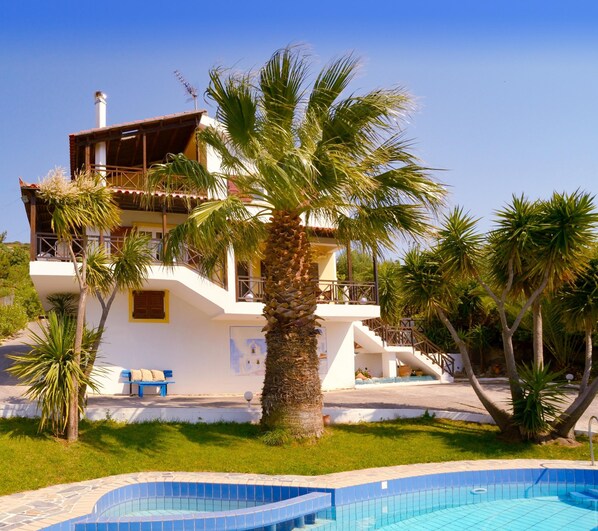 Stunning villa surrounded by lush greenery, featuring a balcony and a pool.