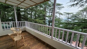 Ein Balkon mit weißer Reling, zwei Stühlen und Blick auf dichten Wald.