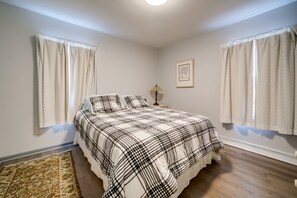 A bedroom with a bed, curtains, a rug, a nightstand, and a wall-mounted lamp.