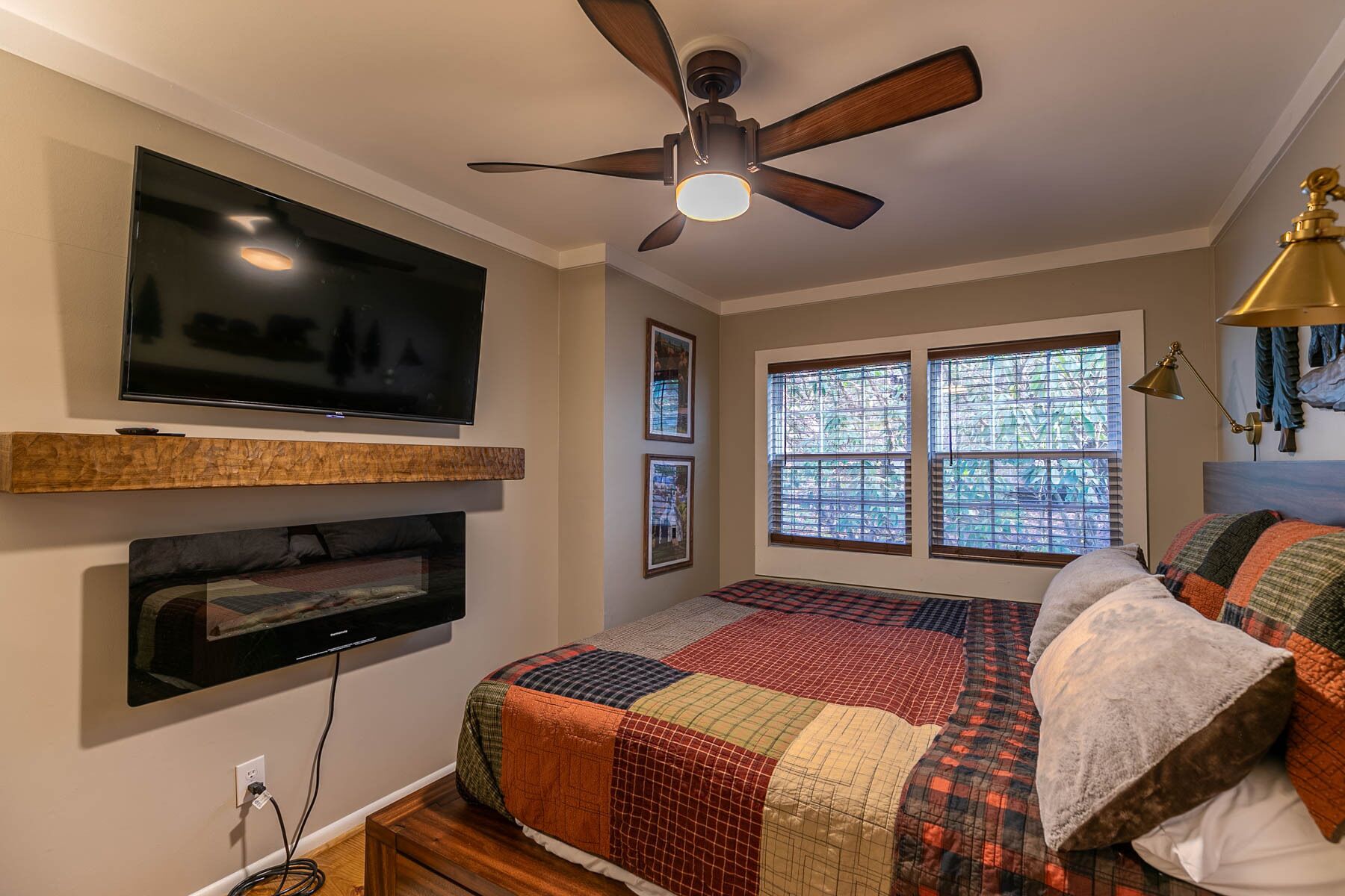 A bedroom with a bed, a ceiling fan, a TV mounted on the wall, and a window with blinds.