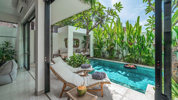 A modern pool area with lounge chairs and a small table, surrounded by lush greenery and a clear blue pool. - Puri Senang - Modern 4BR Pool Villa · Central Berawa · 6 min to Beach & Finns (Canggu)