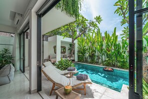 A modern pool area with lounge chairs and a small table, surrounded by lush greenery and a clear blue pool. - Puri Senang - Modern 4BR Pool Villa · Central Berawa · 6 min to Beach & Finns (Canggu)
