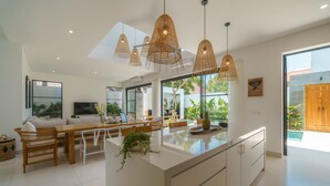 A modern kitchen with a central island, pendant lights, and a view of the outdoors. - Puri Senang - Modern 4BR Pool Villa · Central Berawa · 6 min to Beach & Finns (Canggu)