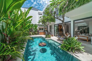 Ett modernt hus med en swimmingpool, omgivet av frodig grönska.
