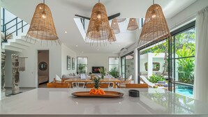 A modern kitchen with a central island, dining area, and a view of a swimming pool. - Puri Senang - Modern 4BR Pool Villa · Central Berawa · 6 min to Beach & Finns (Canggu)