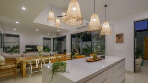 A modern kitchen with a central island, dining area with wooden furniture, and hanging rattan lights. - Puri Senang - Modern 4BR Pool Villa · Central Berawa · 6 min to Beach & Finns (Canggu)