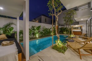 Ett modernt utomhuspoolområde med solstolar, en liten pool och frodig grönska.