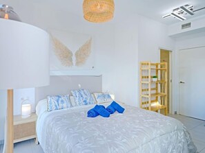 A bedroom with a bed, a nightstand, a lamp, a wall-mounted shelf, and a door. - Calpe Beach II by Interhome (Calpe/Calp)