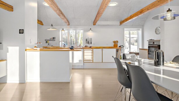 A modern kitchen with wooden beams, a central island, and a dining area with chairs. - 3 bedroom stunning home in Løkken (Løkken)