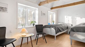 A modern bedroom with a bed, two chairs, a small table with a lamp, and large windows with plants. - 3 bedroom stunning home in Løkken (Løkken)