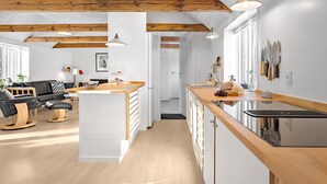 A modern kitchen with wooden beams, a central island, and a dining area with a sofa and chairs. - 3 bedroom stunning home in Løkken (Løkken)