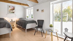 A modern bedroom with a bed, two chairs, a small table, and a large window offering a view of a snowy garden. - 3 bedroom stunning home in Løkken (Løkken)