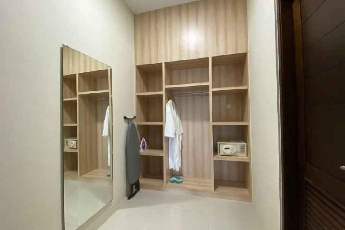 Un couloir mène à un placard en bois doté de plusieurs étagères et d’un miroir.