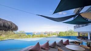 A poolside area with wooden deck, seating, and a view of the ocean. - ZASGO HOTEL (Labuan Bajo)