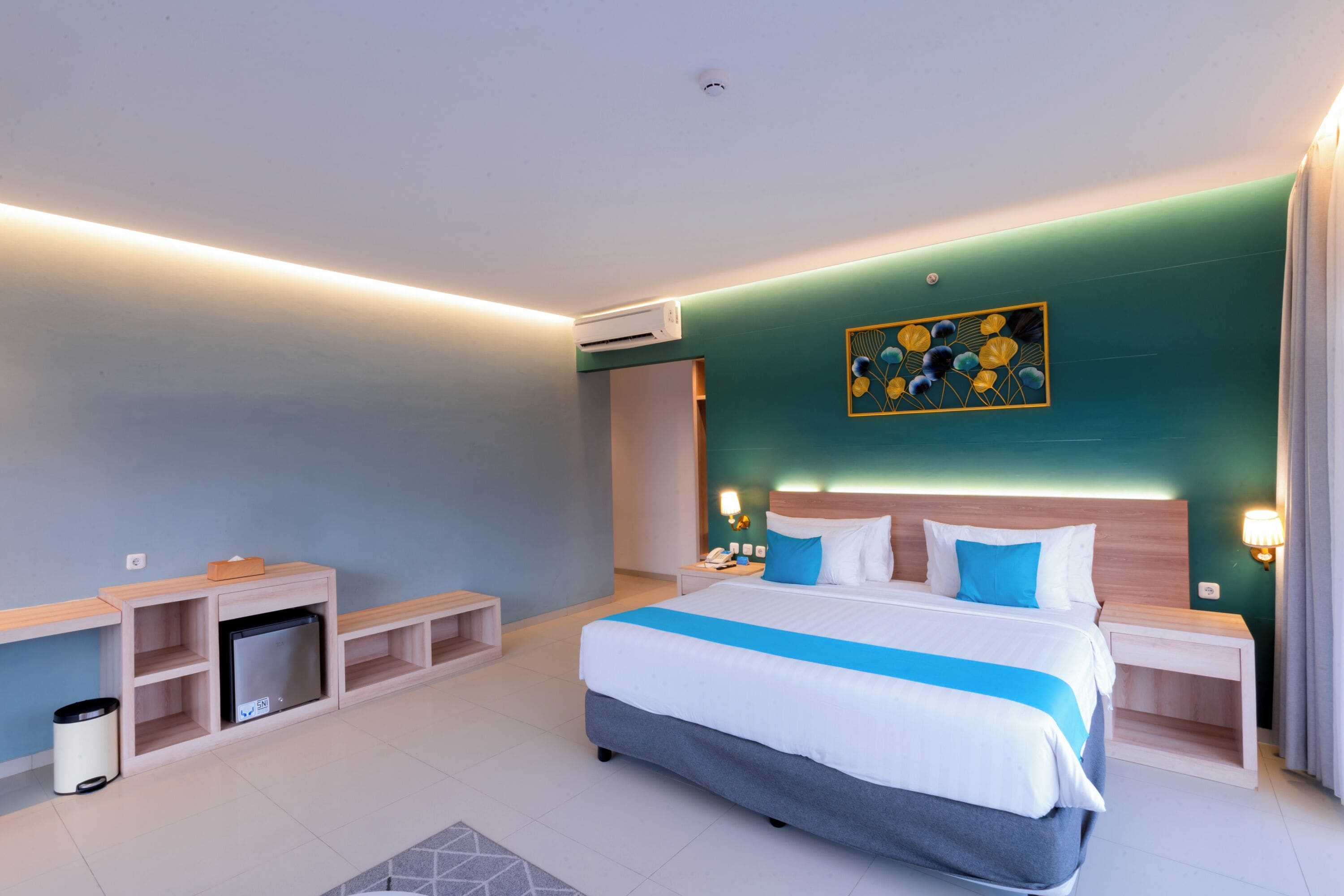 A modern hotel room with a large bed, bedside tables, a small desk, and a wall-mounted air conditioner.