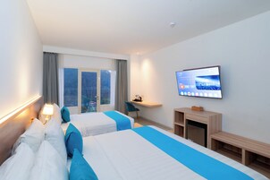 A hotel room with two beds, a TV, a desk, and a view of the city.