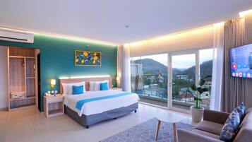 Quarto de hotel moderno com uma cama grande, um sofá, uma televisão e uma varanda com vista para a cidade.