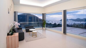 A modern living room with a large window, a sofa, two small tables, and a potted plant. - ZASGO HOTEL (Labuan Bajo)