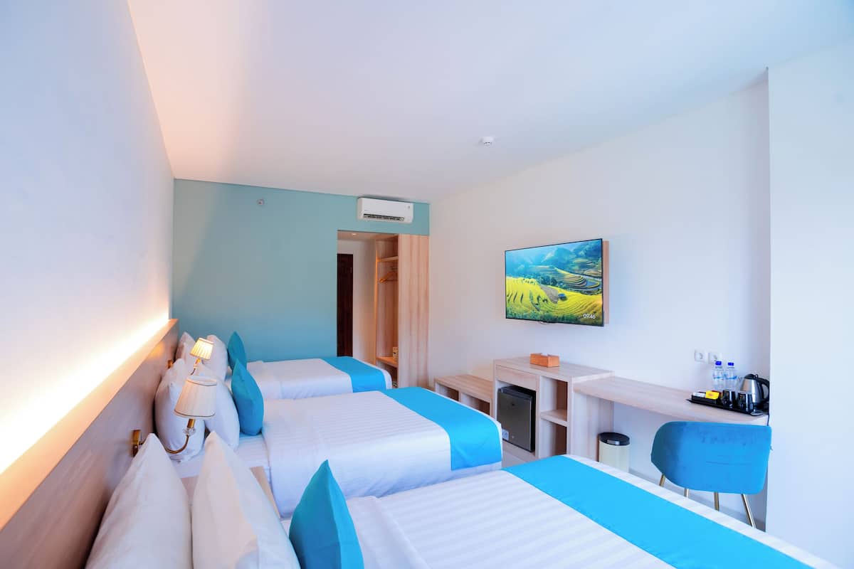 A hotel room with two beds, a desk, a chair, a TV, and an air conditioning unit.