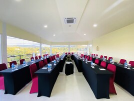 Un salón de conferencias con mesas largas, sillas rojas y botellas de agua.