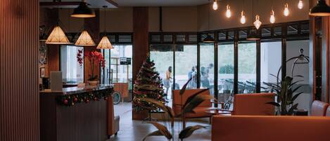 A modern hotel lobby with a reception desk, seating area, large windows, and a decorated Christmas tree.