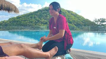 A person in a red shirt sitting by a pool with a mountain in the background.